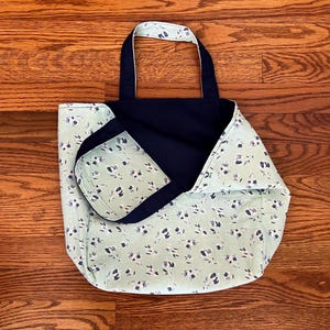 Pode incluir: Uma bolsa tote revers&iacute;vel com um tecido verde menta claro com um padr&atilde;o floral pequeno em azul escuro e branco de um lado e um tecido azul-marinho s&oacute;lido do outro, completa com duas al&ccedil;as de ombro de tecido a condizer.