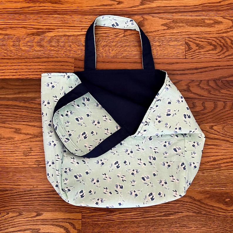 Pode incluir: Uma bolsa tote revers&iacute;vel com um tecido verde menta claro com um padr&atilde;o floral pequeno em azul escuro e branco de um lado e um tecido azul-marinho s&oacute;lido do outro, completa com duas al&ccedil;as de ombro de tecido a condizer.