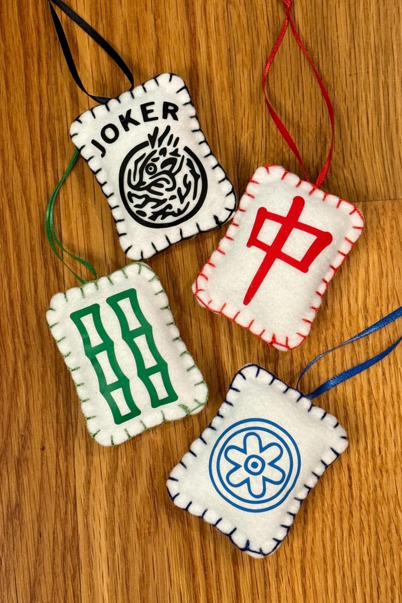 May include: Four white felt ornaments with stitched edges and ribbon hangers. Each ornament features a different design in black, green, red, and blue. One says "JOKER" with a black graphic. Others have Chinese symbols and a flower.