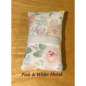 Pode incluir: Uma almofada retangular de pel&uacute;cia com um fundo branco macio e um delicado padr&atilde;o floral em tons de rosa, p&ecirc;ssego e verde s&aacute;lvia. Uma faixa larga de tecido branco liso est&aacute; posicionada horizontalmente no centro da almofada.