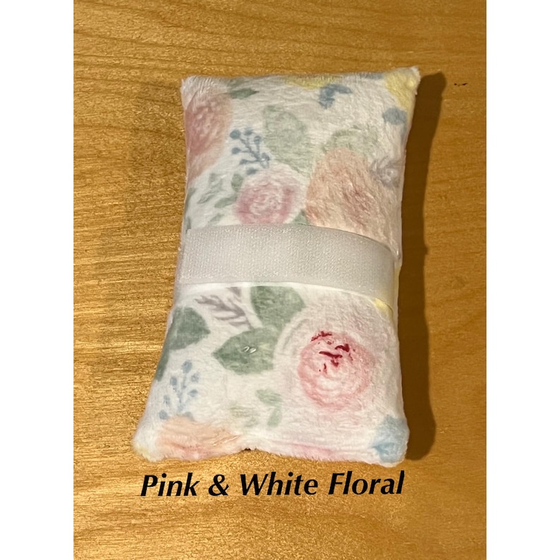 Pode incluir: Uma almofada retangular de pel&uacute;cia com um fundo branco macio e um delicado padr&atilde;o floral em tons de rosa, p&ecirc;ssego e verde s&aacute;lvia. Uma faixa larga de tecido branco liso est&aacute; posicionada horizontalmente no centro da almofada.