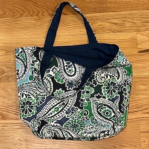 Pode incluir: Uma bolsa tote com um padr&atilde;o paisley em azul escuro, verde e branco. A bolsa tem duas al&ccedil;as de tecido azul escuro e um forro interior azul escuro s&oacute;lido. O tecido exterior apresenta um design denso e repetitivo de flores e paisley.