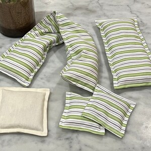 May include: Five striped fabric heat packs, two are long and rectangular, two are square, and one is a long, narrow neck wrap. The neck wrap is folded in half. All are made of white fabric with green and purple stripes.