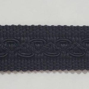 May include: Black decorative trim with a looped design along the top edge. The trim has a woven texture and is suitable for various craft and sewing projects. The trim is a solid black color.