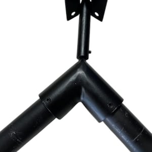 May include: Black metal corner bracket with a hinge and mounting plate. The bracket is designed to connect two pieces at a 90-degree angle. The hinge allows for movement.