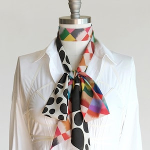 May include: A white shirt with a black and white polka dot and colorful geometric patterned scarf tied around the neck.