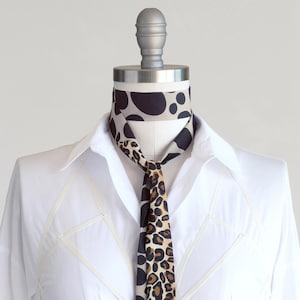 May include: A white collared shirt with a black and brown leopard print scarf tied around the neck.