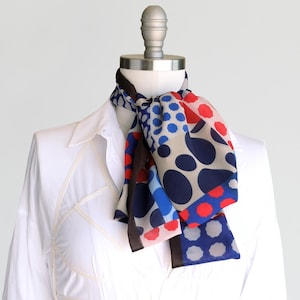 May include: A white shirt with a colorful polka dot scarf tied around the neck. The scarf is made of a light fabric and has a pattern of red, blue, and white polka dots.