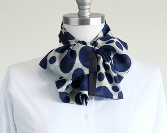 May include: A white collared shirt with a navy blue and white polka dot bow tie. The bow tie is tied in a loose knot and has a black ribbon in the centre.