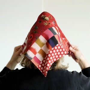 May include: A person wearing a black shirt with a red, white and blue patterned headscarf. The headscarf features a variety of geometric and floral designs.