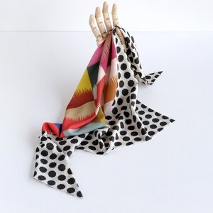 Puede incluir: Una bufanda estampada de colores con lunares negros. La bufanda est&aacute; drapeada sobre una mano de madera.