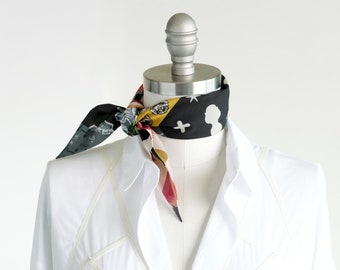 May include: A white button-down shirt with a decorative white stitching design. The shirt has a black and yellow patterned scarf tied around the collar.