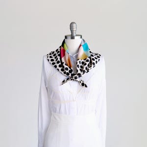Puede incluir: Una camisa blanca de manga larga con una bufanda de lunares negros y blancos con patrones geom&eacute;tricos coloridos.