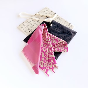 Puede incluir: Un pa&ntilde;uelo de seda con estampado rosa y beige sobre una tela con estampado blanco y negro. El pa&ntilde;uelo est&aacute; atado con una cinta blanca.