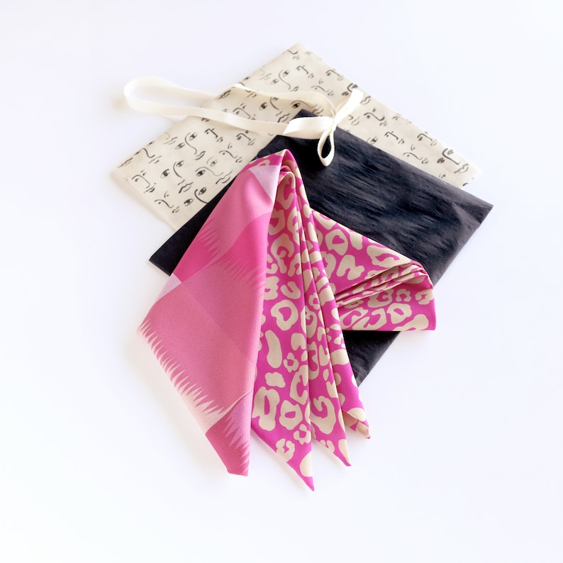 Puede incluir: Un pa&ntilde;uelo de seda con estampado rosa y beige sobre una tela con estampado blanco y negro. El pa&ntilde;uelo est&aacute; atado con una cinta blanca.