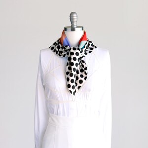 Puede incluir: Una camisa blanca con una bufanda de lunares blancos y negros atada alrededor del cuello. La bufanda tiene un patr&oacute;n geom&eacute;trico colorido en la parte posterior.