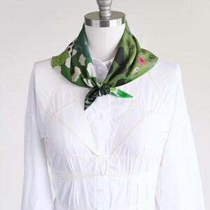 Small soft triangle scarf in a fun medley of green prints. Shown tied in a sailor style on a mannequin in a white dress.