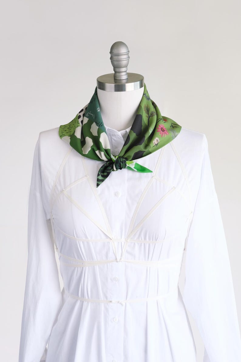 Small soft triangle scarf in a fun medley of green prints. Shown tied in a sailor style on a mannequin in a white dress.