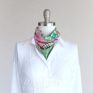 A pretty pink and green patchwork print small triangle scarf tied in a bib and tucked into a white shirt as an ascot.