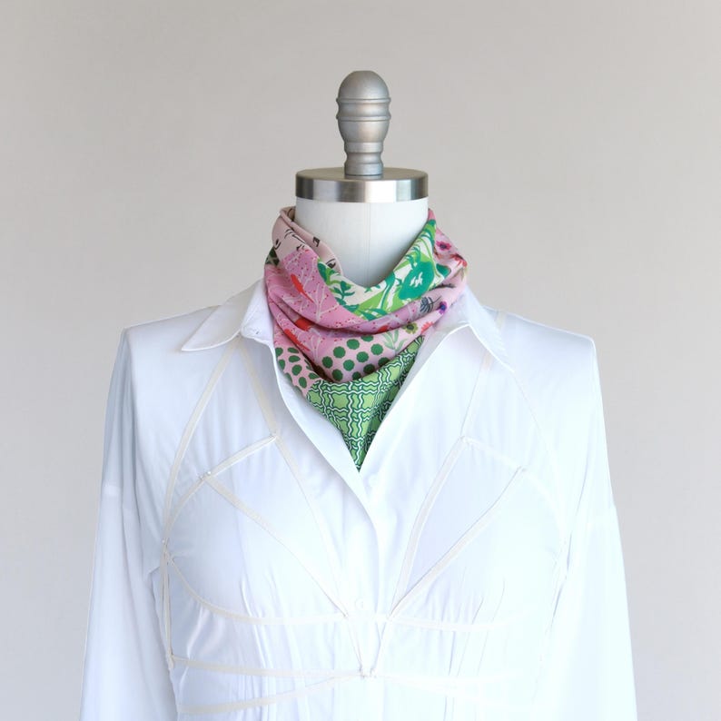 A pretty pink and green patchwork print small triangle scarf tied in a bib and tucked into a white shirt as an ascot.