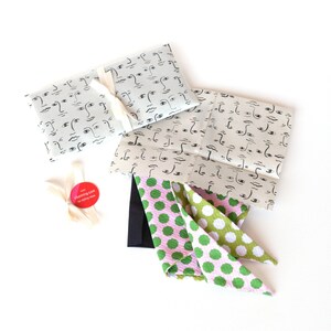 K&ouml;nnte beinhalten: Zwei Geschenkpapierdesigns mit einem Muster aus schwarzen und wei&szlig;en Gesichtern. Ein rosa-gr&uuml;nes gepunktetes Stoffst&uuml;ck liegt auf dem Papier.