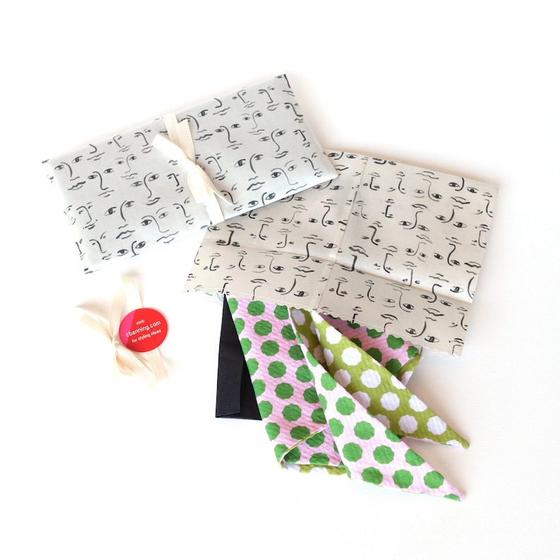 K&ouml;nnte beinhalten: Zwei Geschenkpapierdesigns mit einem Muster aus schwarzen und wei&szlig;en Gesichtern. Ein rosa-gr&uuml;nes gepunktetes Stoffst&uuml;ck liegt auf dem Papier.
