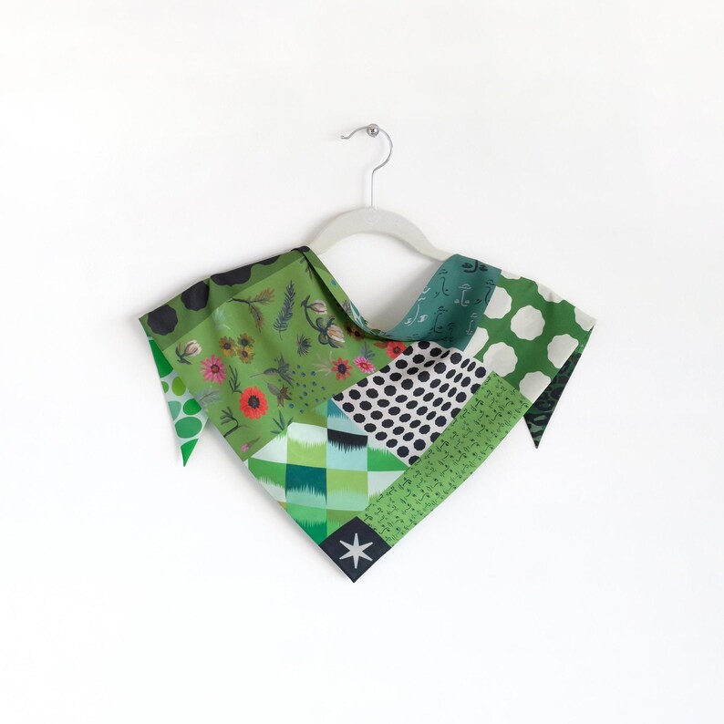K&ouml;nnte beinhalten: Ein Patchwork-Schal mit einer Vielzahl von gr&uuml;nen Mustern, darunter Blumen, Polka Dots und geometrische Designs. Der Schal wird auf einem wei&szlig;en Kleiderb&uuml;gel vor einem wei&szlig;en Hintergrund pr&auml;sentiert. Das Design des Schals enth&auml;lt einen Stern.