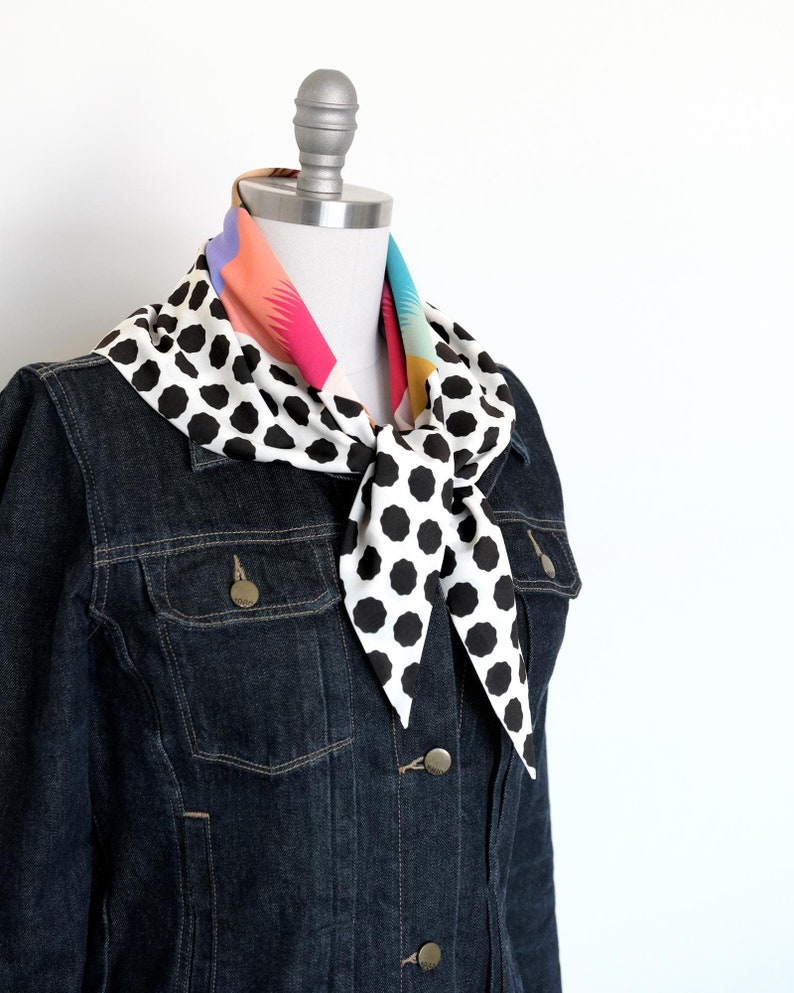 This image showcases a colorful mod check and black and white dot print triangle scarf tied with a single loop around the neck of a mannequin in a dark denim jacket.