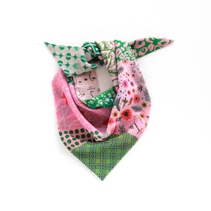 May include: A colorful silk scarf with a patchwork design. The scarf features sections of pink, green, and white with various patterns, including floral, geometric, and abstract face designs. The scarf is tied in a knot.