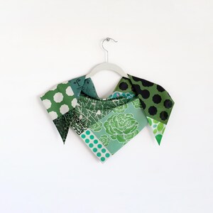 One side of a green patchwork print small triangle scarf draped over a hanger.