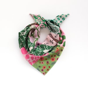 May include: A colorful square scarf with a variety of patterns. The scarf features sections of pink polka dots, green floral designs, and green and pink abstract patterns. The scarf is tied at the top.