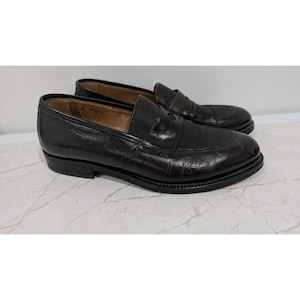 May include: A pair of dark brown leather loafers featuring a textured fabric panel across the vamp and a low heel. The shoes have a smooth leather finish on the sides and a rounded toe design with visible stitching along the sole and upper edge.