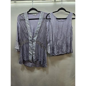 Könnte beinhalten: Ein lavendelfarbenes zweiteiliges Set bestehend aus einem ärmellosen Top und einer passenden langärmeligen Strickjacke mit offener Vorderseite. Beide Kleidungsstücke haben ein florales Ton-in-Ton-Muster, die Jacke hat einen Verschluss.