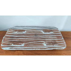 May include: A rectangular glass tray featuring a textured, wood-grain pattern in shades of brown and clear glass. The surface has raised, horizontal ridges mimicking the appearance of timber. A small circular sticker reads Pier 1 Imports.
