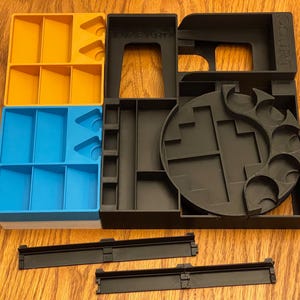 Puede incluir: Un organizador multicompartimento en amarillo, azul y negro. El organizador tiene varias secciones y formas, incluyendo ranuras rectangulares y triangulares, y un diseño circular. La palabra "COURT" es visible en una sección. También se incluyen dos rieles negros.