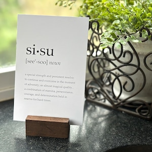 May include: A white card with the word "si.su" and its pronunciation, "see'-soo", printed in black. The word is defined as "a special strength and persistent resolve to continue and overcome in the moment of adversity; an almost magical quality... a combination of stamina, perseverance, courage, and determination held in reserve for hard times."