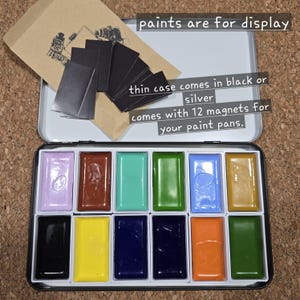 May include: A silver watercolor paint case with 12 colorful paint pans. The case includes 12 magnets for paint pans. The text on the image says "paints are for display" and "thin case comes in black or silver".