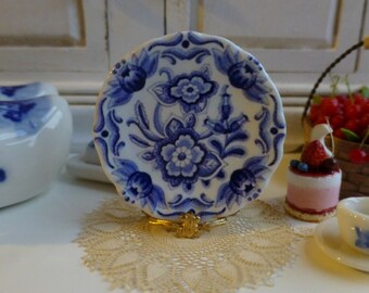 Op de afbeelding: Een blauw en wit porseleinen bord met een bloemenmotief. Het bord staat op een gouden standaard en een wit kantje.