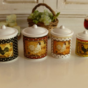 以下が含まれることがあります： 黒、赤、黄色の水玉模様と、雄鶏と雌鶏のイラストが描かれた白いセラミック製のキャニスターが4つ。キャニスターは白い表面の上に置かれています。