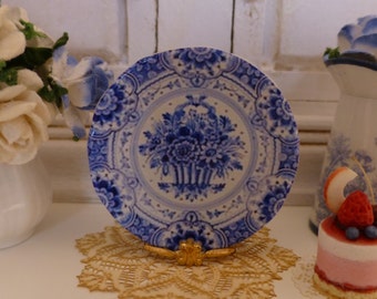 May include: A blue and white porcelain plate with a floral design. The plate is on a gold stand and has a delicate, intricate pattern.