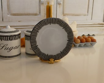 May include: A white ceramic plate with a black and white checkered border, displayed on a gold stand. Two matching sugar jars with black trim and the word "Sugar" are also visible. A carton of eggs is in the background.