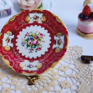 May include: A miniature red and gold porcelain plate with a floral design, a miniature bottle of wine, a miniature glass of wine, a miniature cake with a strawberry on top, and a miniature key.