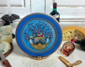 May include: A blue and gold decorative plate with a seashell design and a coral branch. The plate is on a stand.