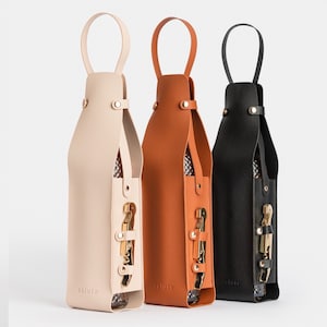 May include: Three leather wine bottle carriers in beige, brown, and black with a gold-colored bottle opener attached to each. The carriers have a handle at the top and the word "saluto" is printed on the bottom of each carrier.