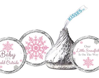 May include: A silver foil-wrapped chocolate candy with a white paper banner that says "Kisses". Three circular stickers with snowflake designs and text that reads "Baby it's cold outside" and "Our Little Snowflake Is On The Way".