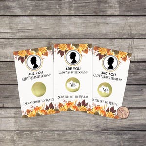 May include: Three scratch-off cards with the text "ARE YOU LADY WHISTLEDOWN?" and a silhouette. One card says "YES", another says "NO". The cards have a floral design and are on a wooden surface.