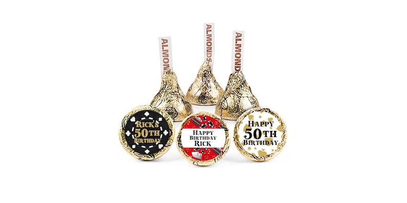 K&ouml;nnte beinhalten: Hershey's Kisses-Pralinen mit goldener Folie und Mandel-Etiketten. Drei stehen aufrecht, drei liegen, jeweils mit einem individuellen Etikett. Die Etiketten lauten "Ricks 50. Geburtstag" oder "Alles Gute zum Geburtstag Rick".