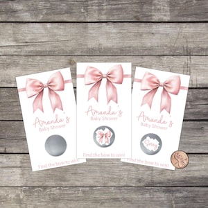 May include: Three baby shower scratch-off cards with a pink bow design. Each card reads "Amanda's Baby Shower" and "Find the bow to win!". One card has a "Sorry" message. A penny is next to the cards.