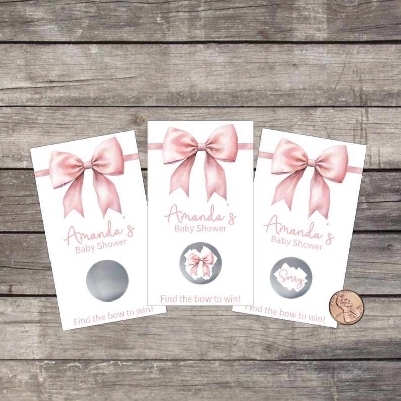 May include: Three baby shower scratch-off cards with a pink bow design. Each card reads "Amanda's Baby Shower" and "Find the bow to win!". One card has a "Sorry" message. A penny is next to the cards.
