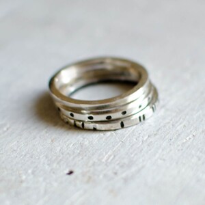 May include: Three silver rings stacked on top of each other. The rings are decorated with small black dots and lines.